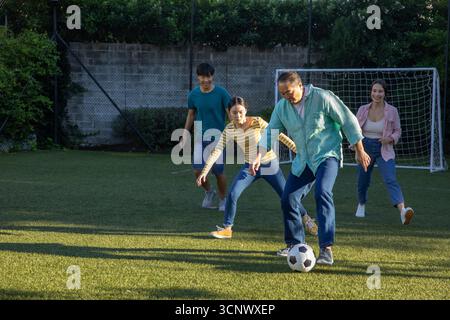 Famiglie diverse che giocano a calcio su un campo in erba vicino a un muro di mattoni con palla da calcio e rete da porta Foto Stock