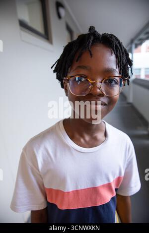 Ragazzo afroamericano in età scolare in piedi in un passaggio coperto con occhiali da vista Foto Stock