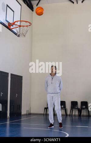 Allenatore maschile in piedi sul campo da basket con cappuccio, fischiare mentre il basket scende verso il cerchio Foto Stock