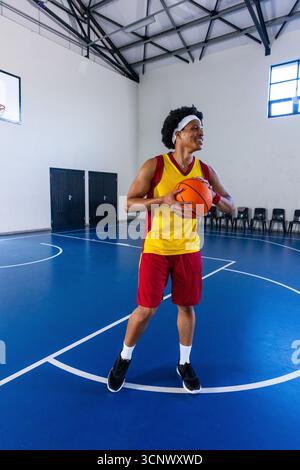 Giocatore afroamericano maschile di basket in maglia gialla in piedi sul campo con palla in mano Foto Stock