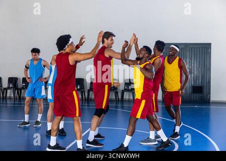 Diversi giocatori maschili di basket in uniformi rosse-gialle, in campo vicino alle sedie Foto Stock