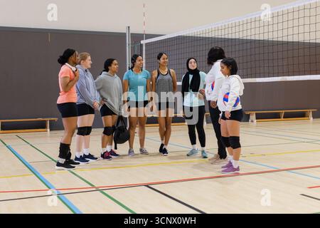 Diverse compagne di squadra di pallavolo che ricevono la guida dell'allenatore in palestra vicino alla rete e alla borsa da pallavolo Foto Stock