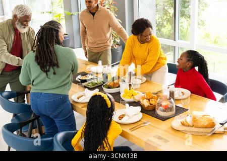 Diverse famiglie multigenerazionali che si riuniscono intorno al tavolo nella sala da pranzo, servendo pollame arrosto Foto Stock