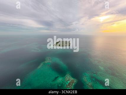 Vista aerea dell'isola di Mucura circondata dal Mar dei Caraibi, catturata durante un sereno tramonto. Le vibranti acque turchesi contrastano con la lussureggiante folia verde Foto Stock