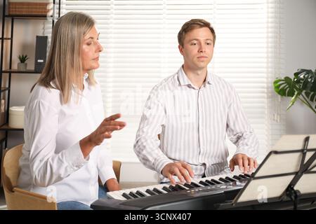 Tutore che insegna all'uomo a suonare il pianoforte al chiuso Foto Stock