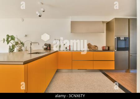 Una cucina moderna ed elegante con mobili arancioni vibranti, elettrodomestici eleganti e una disposizione pulita e minimalista, perfetta per un soggiorno contemporaneo Foto Stock