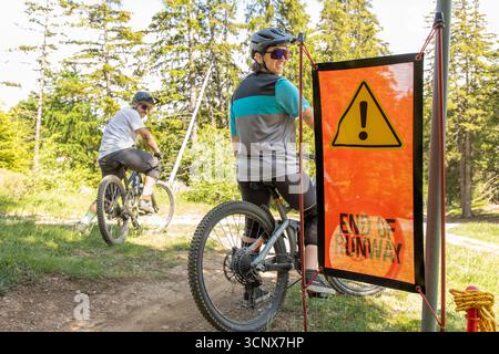 Due mountain bike si fermano in un punto finale con un cartello di avvertimento in un'area boschiva. La giornata di sole evidenzia la bellezza naturale di Crans-Montana, un populista Foto Stock