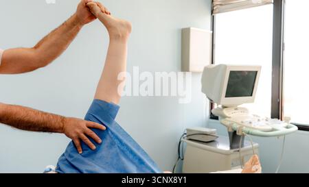 Il fisioterapista maschile non riconoscibile ritagliato assiste una paziente senza volto nell'esecuzione di esercizi di riabilitazione in un ambiente clinico per physica Foto Stock