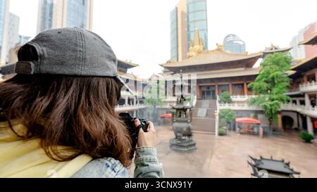 Un visitatore cattura l'antica architettura del Tempio di Jing'an, un importante tempio buddista a Shanghai, in Cina, che contrasta splendidamente con il moderno Foto Stock