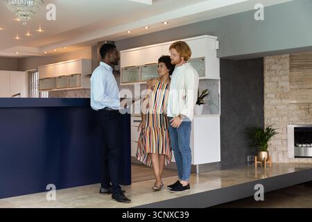 Gruppi diversi che visitano la cucina moderna vicino all'isola marina con un agente che tiene in mano gli appunti Foto Stock