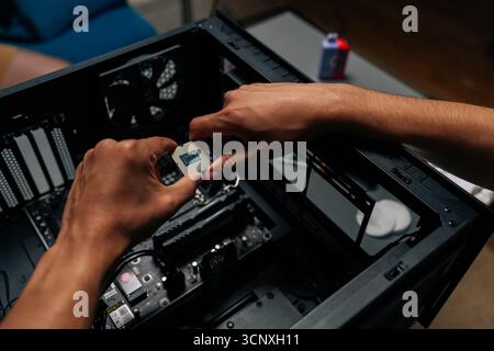 Vista dall'alto del tecnico non riconoscibile che inserisce il processore nella scheda madre per sistemi desktop durante il processo di aggiornamento o riparazione dell'hardware del computer in un'officina buia Foto Stock