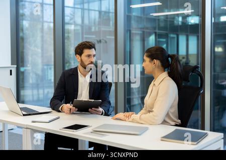 Responsabile delle risorse umane che conduce un importante colloquio di lavoro con una candidata in un ufficio aziendale contemporaneo, discutendo di potenziali opportunità di lavoro e di carriera Foto Stock