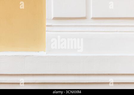 Una parete esterna pulita e luminosa caratterizzata da un pannello giallo tenue e intonaco bianco con modanatura decorativa e sporgenze stratificate. Tranquillo, moderno e architettonico Foto Stock