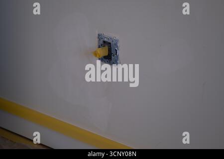 Primo piano del foro della presa elettrica coperto con nastro giallo su parete bianca durante il processo di riparazione e ristrutturazione. Ottimo per il fai da te, l'edilizia, la sicurezza, i Foto Stock