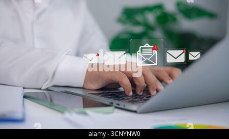 Primo piano di un uomo d'affari che digita sul laptop con più icone di notifica e-mail e simbolo di avviso, concetto di comunicazione digitale, messaggistica aziendale Foto Stock