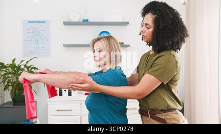 Il fisioterapista assiste una donna anziana nell'esercizio del braccio utilizzando la banda di resistenza durante la sessione di terapia Foto Stock