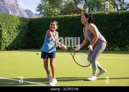 Madre e figlia asiatiche che fanno oscillare le racchette da tennis mentre giocano su un campo privato da giardino Foto Stock