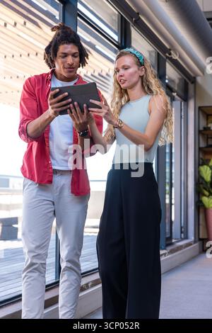 Colleghi diversi in abbigliamento aziendale che puntano al piano di revisione dei dispositivi tablet in ufficio per finestre Foto Stock