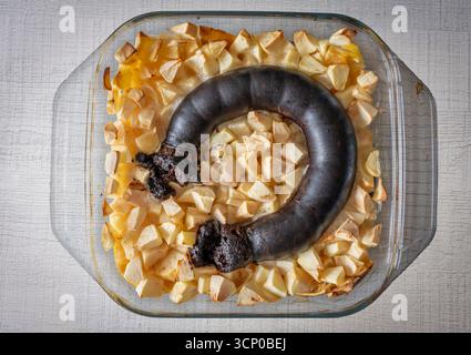 Piatto fatto in casa. Un piatto di vetro con un pezzo di budino nero tagliato e composta di mele Foto Stock