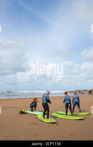 Allenamento di surf con istruttore e allievi o allievi maschi e femmine sulla spiaggia di Bude, sulla costa nord della Cornovaglia. Foto Stock