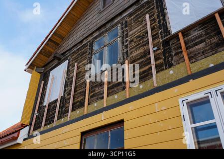 Primo piano di una vecchia casa in legno in fase di ristrutturazione con nuovi rivestimenti gialli, isolanti e miglioramenti delle finestre Foto Stock