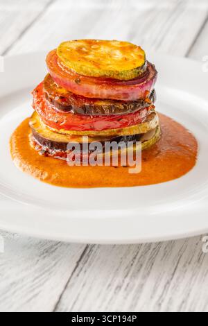 Verdure ratatouille al forno impilate in una torre vibrante, con strati dorati messi in risalto splendidamente Foto Stock
