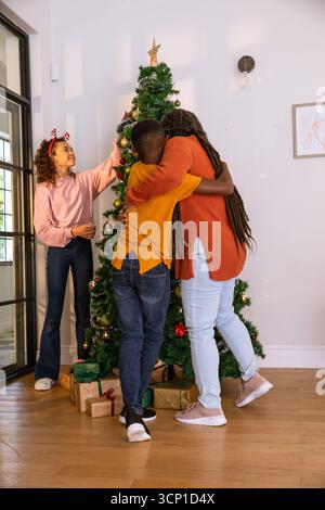 Famiglia afroamericana che decora l'albero di natale in soggiorno con regali e fascia per renne Foto Stock