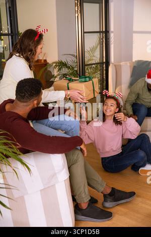 Diverse famiglie che si scambiano articoli da regalo confezionati con fasce e cappello di babbo natale in soggiorno, spazio copie Foto Stock