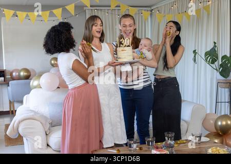 Diverse amiche che festeggiano il 30° compleanno a casa applaudono vicino a torte, palloncini, neonati Foto Stock