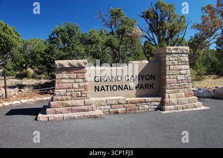 Cartello di ingresso in pietra del Parco Nazionale del Grand Canyon in una giornata di sole, circondato da alberi verdi e cielo blu, che accoglie i visitatori in Arizona Foto Stock