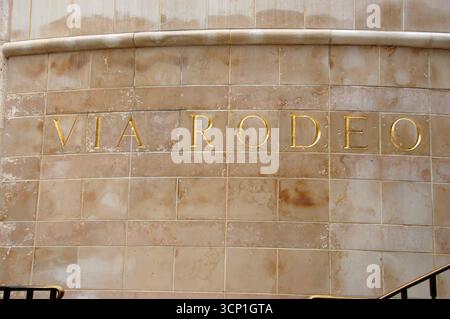 Iscrizione dorata "VIA RODEO" su un muro di marmo beige nel famoso quartiere dello shopping di Beverly Hills, simbolo di lusso, moda ed esclusività Foto Stock
