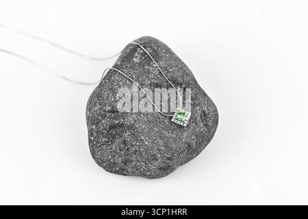 Una collana è sopra una roccia. La collana è argento e verde. La roccia è grigia e ruvida Foto Stock