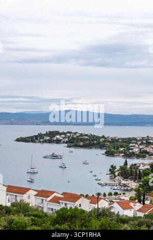 Una tranquilla scena costiera caratterizzata da case bianche con tetti rossi lungo una costa, vegetazione lussureggiante in primo piano e barche ancorate in un blu tranquillo Foto Stock