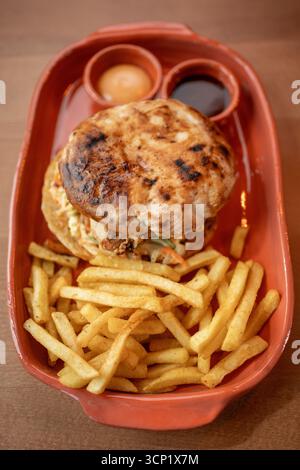 Gustoso sandwich di pollo arrosto servito con patatine fritte e salse croccanti Foto Stock