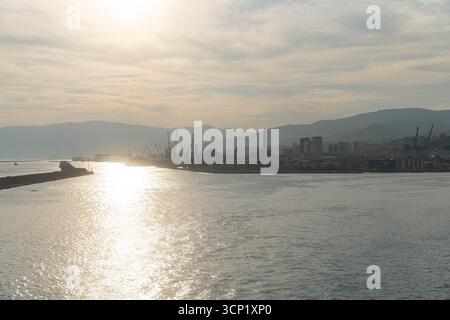 Vista del tramonto sulla baia di Genova con il porto industriale in lontananza. Concetto di viaggio, navigazione, energia e paesaggio mediterraneo. Foto Stock