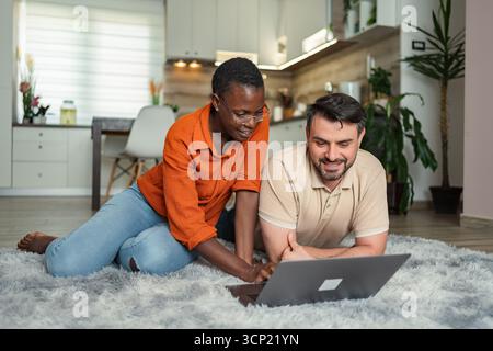 Coppia sdraiata su moquette usando un computer portatile nel soggiorno di casa Foto Stock