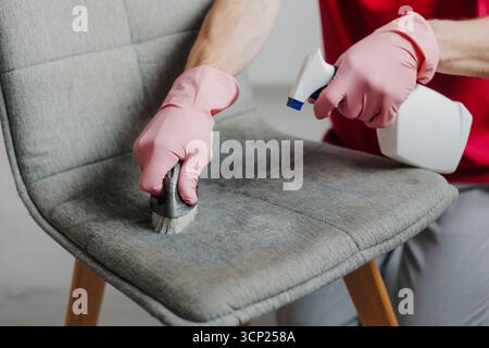 Primo piano dell'uomo utilizzare uno spray detergente per pulire la sedia a casa Foto Stock