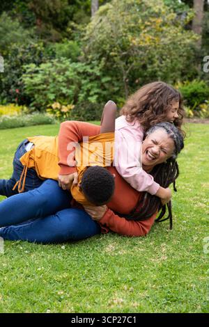 Madre e figli afroamericani che ridono e solleticano l'un l'altro sul prato in giardino Foto Stock