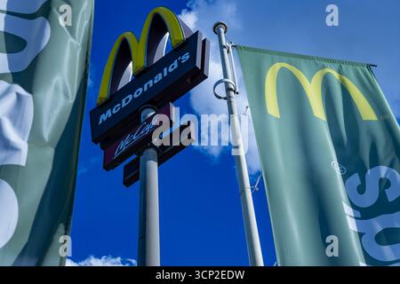 McDonald's e McCafé cartellone pubblicitario con bandiere sventolanti catturate contro un cielo estivo limpido in Germania, prospettiva verso l'alto. Foto Stock