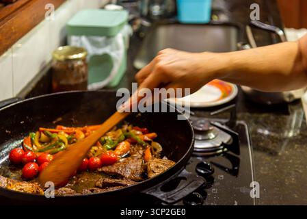 Bistecca con cipolle e pomodori rossi preparati in una cucina residenziale. Foto Stock
