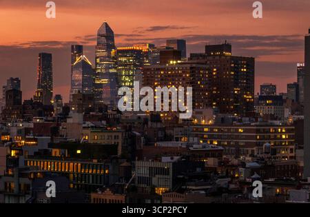 New York, NY - US - 14 settembre 2025 Vista al tramonto dello skyline di Manhattan con grattacieli illuminati e luci scintillanti della città, ambientata in un'orang drammatica Foto Stock