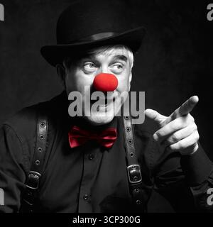 Ritratto a colori selettivo di clown ridendo. Un uomo anziano con naso rosso da clown e cappello da bowler sulla testa. Vestito in camicia nera con bretelle. Il clo Foto Stock