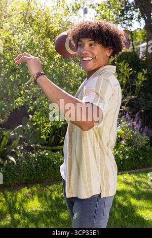 Uomo afroamericano che lancia football nel giardino del cortile con braccialetti Foto Stock