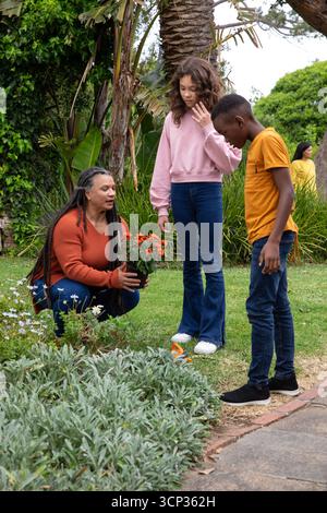 Diverse famiglie si inginocchiano su un prato nel giardino del cortile con piante in fiore in vaso Foto Stock