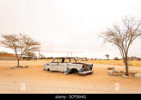 Il cimitero automobilistico di Solitario in Namibia presenta auto d'epoca arrugginite vicino a piccoli edifici desertici, adagiate contro dune e montagne, catturando il fascino del deserto Foto Stock