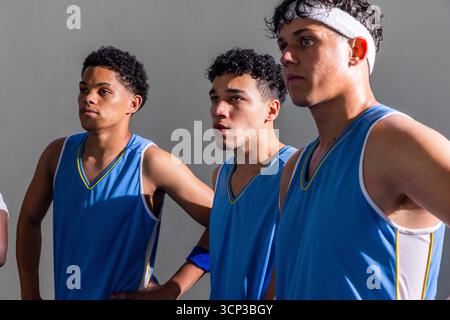 Squadra afroamericana di basket maschile che posa in palestra indossando maglie blu e fascia Foto Stock