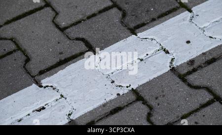 Vista ravvicinata di una linea dipinta di bianco su pietre di pavimentazione incrinate. L'immagine mostra la struttura urbana, la segnaletica stradale e i dettagli delle superfici esterne con vi Foto Stock