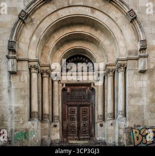 Porta ornata in legno intagliato adagiata in una storica arcata in pietra con colonne classiche e dettagli architettonici romanici Foto Stock