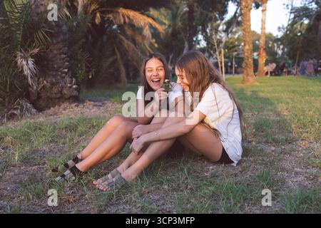 Ritratto di due ragazze sorridenti sedute sull'erba. Ragazze felici che si divertono nel parco Foto Stock