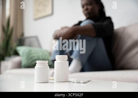 Una donna siede tranquillamente sul divano, a fronteggiare con tristezza il suo ambiente domestico. Foto Stock